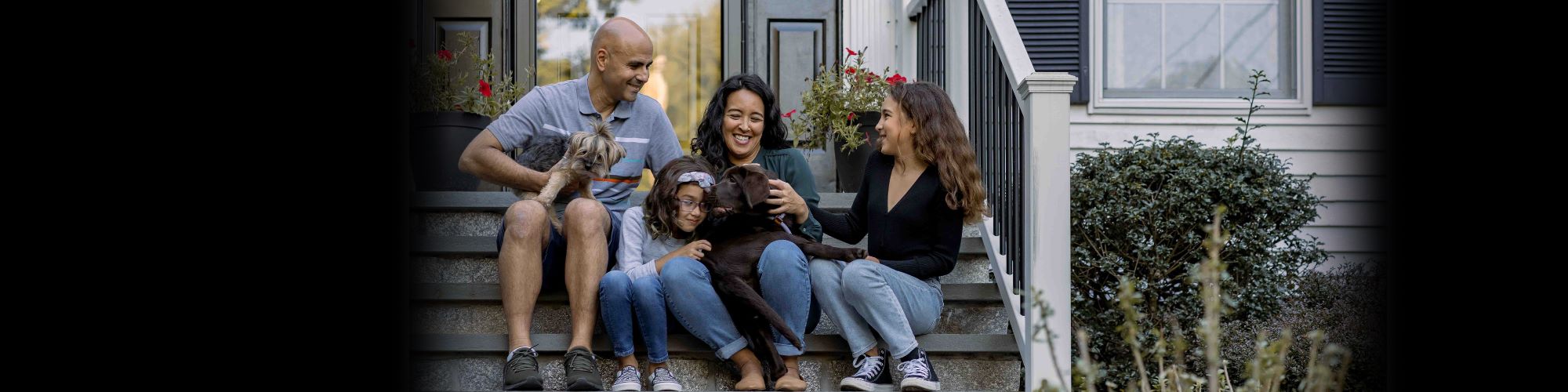 A family of 4 sites on a front door stoop with a dog