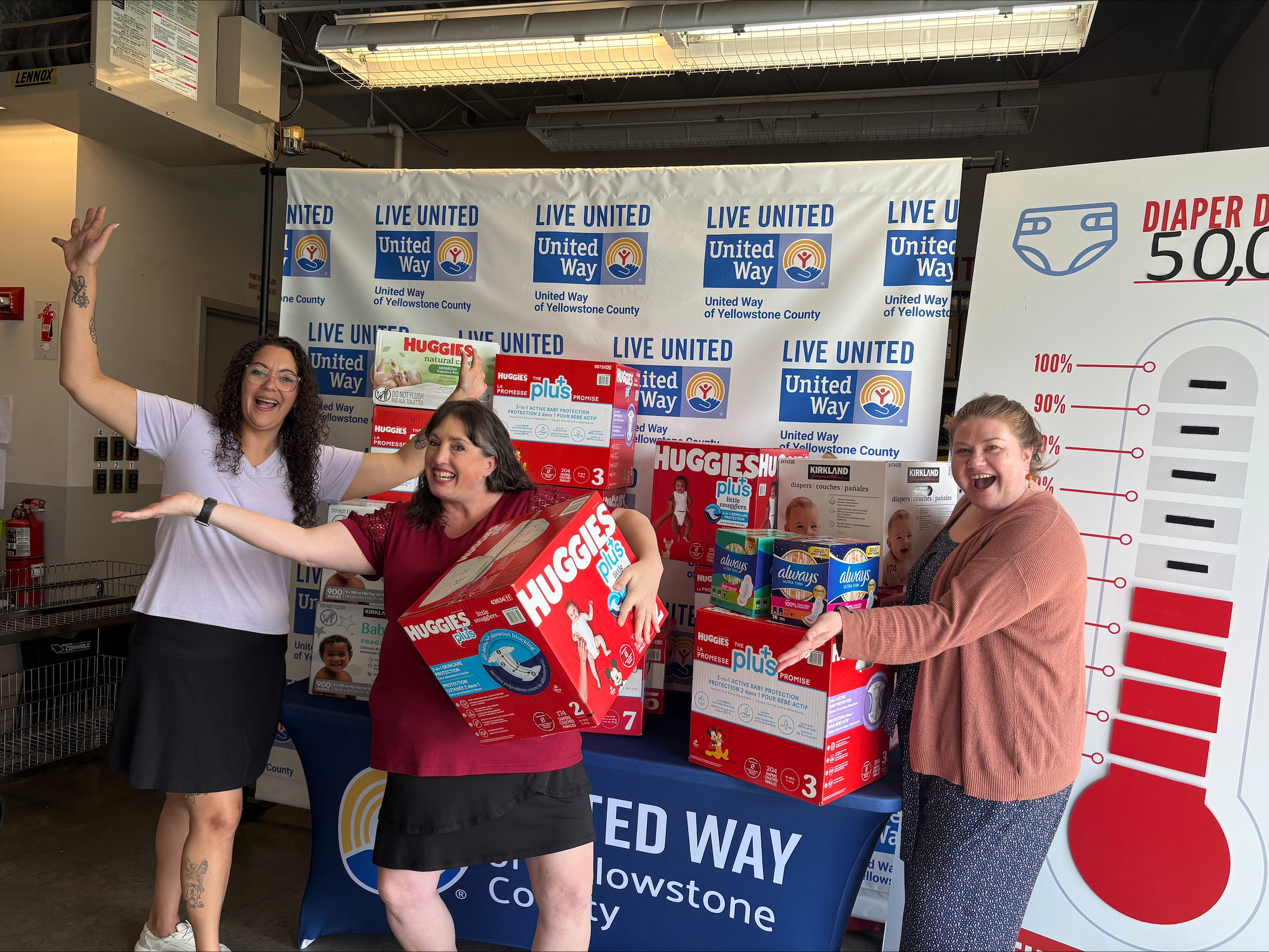 Three women pose alongside a stack of donated diapers.