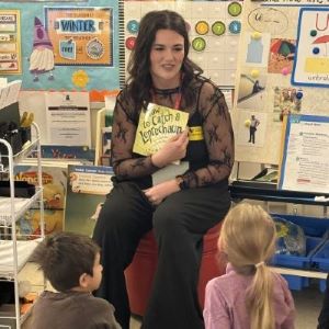 A woman holds up a book she's about to read to a group of children