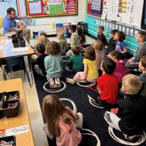 A man reads to a group of children from a book he's holding to his side.