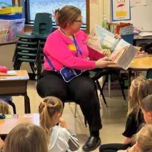 A woman flips a page in a book that she's reading to a group of children
