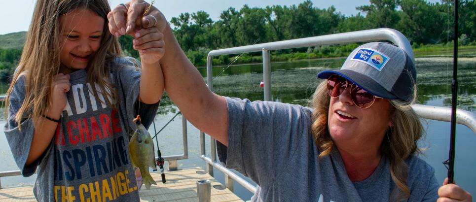 A woman holds a fish on a line with the child who caught it