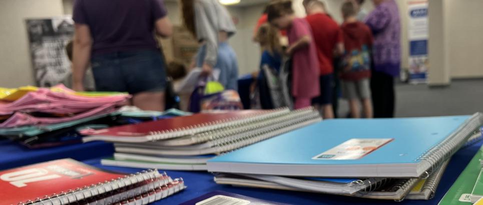 Families browse school supplies behind a table of notebooks