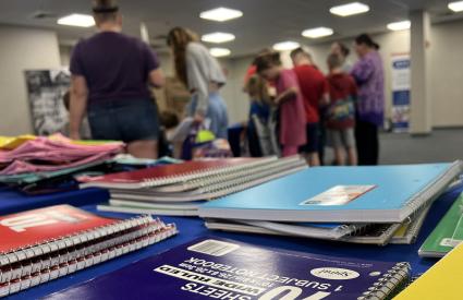 Families browse school supplies behind a table of notebooks
