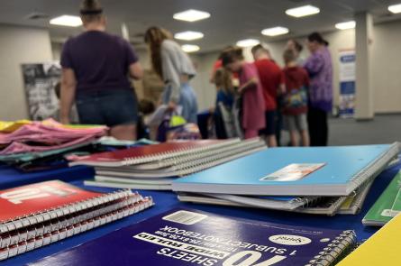 Families browse school supplies behind a table of notebooks