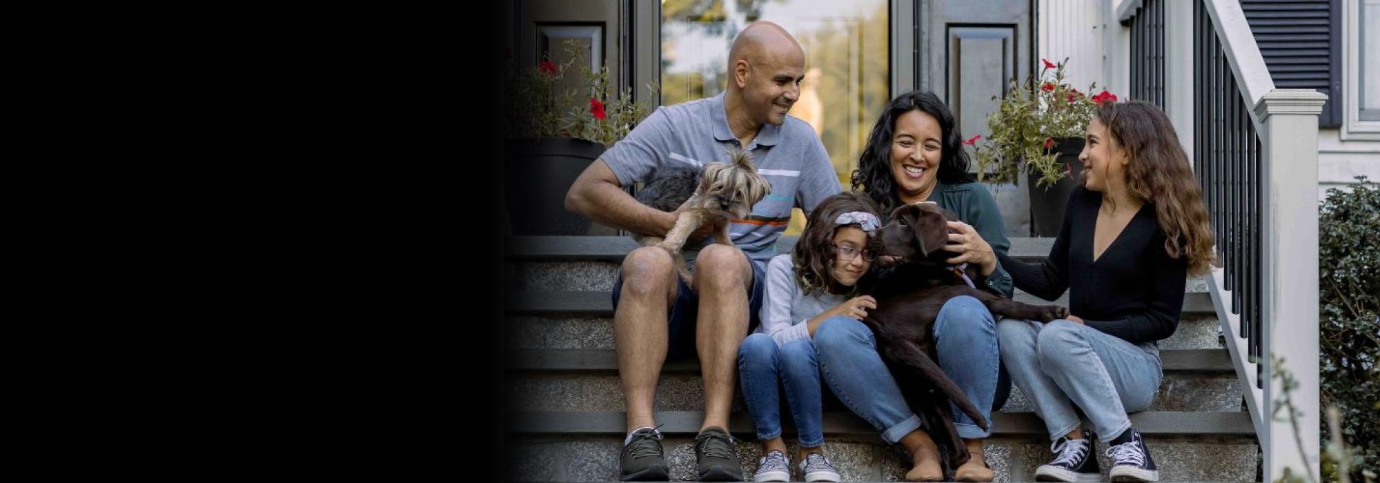 A family of 4 sites on a front door stoop with a dog